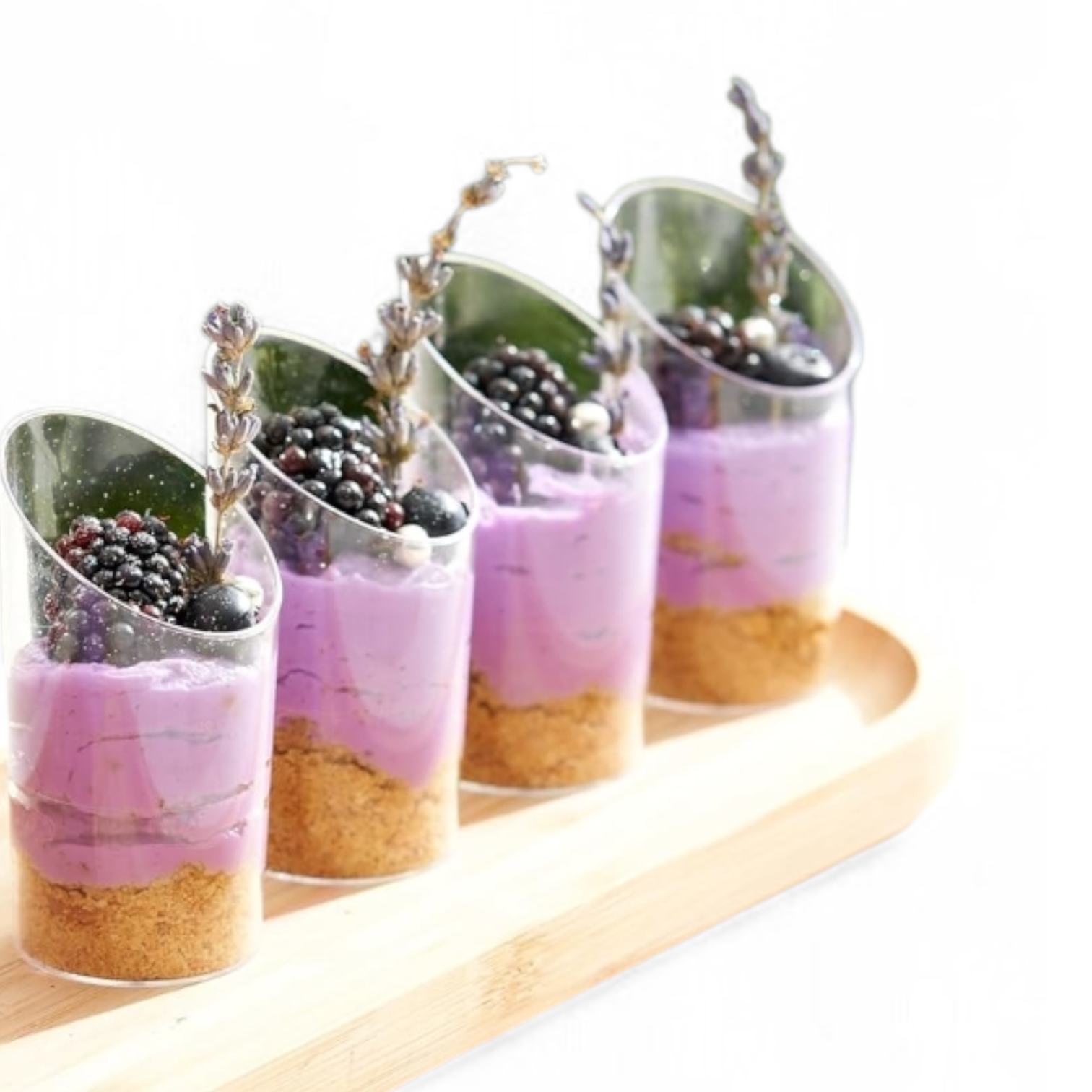 Four dessert cups with purple layers, graham cracker crusts, and berries on a white background.
