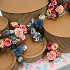 DIY grazing table kit baby shower gender reveal with disposable natural platters plinths, pink and blue flowers, baby footprint confetti and a "girl or boy?" sign detail view - grazekits